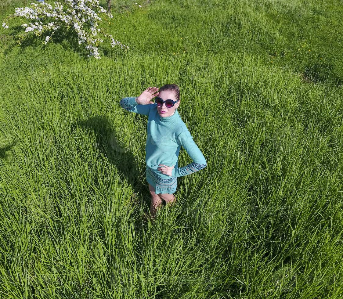 giovane ragazza nel un' leggero verde vestito su il prato con verde erba. Visualizza di un' uomo a partire dal sopra a partire dal un' altezza. foto