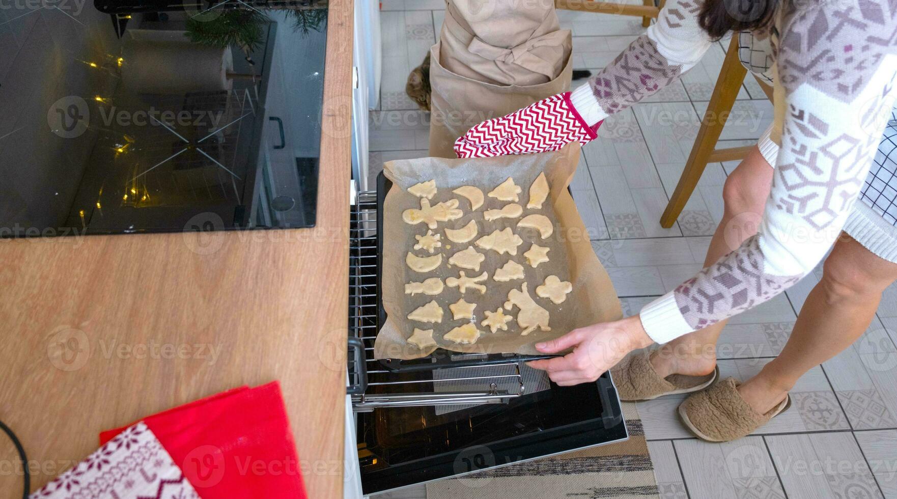 mamma mette ritagliare biscotti nel il forno a partire dal il Impasto con muffe su un' Natale tema nel il modulo di un' pupazzo di neve, un' Natale albero, stelle foto