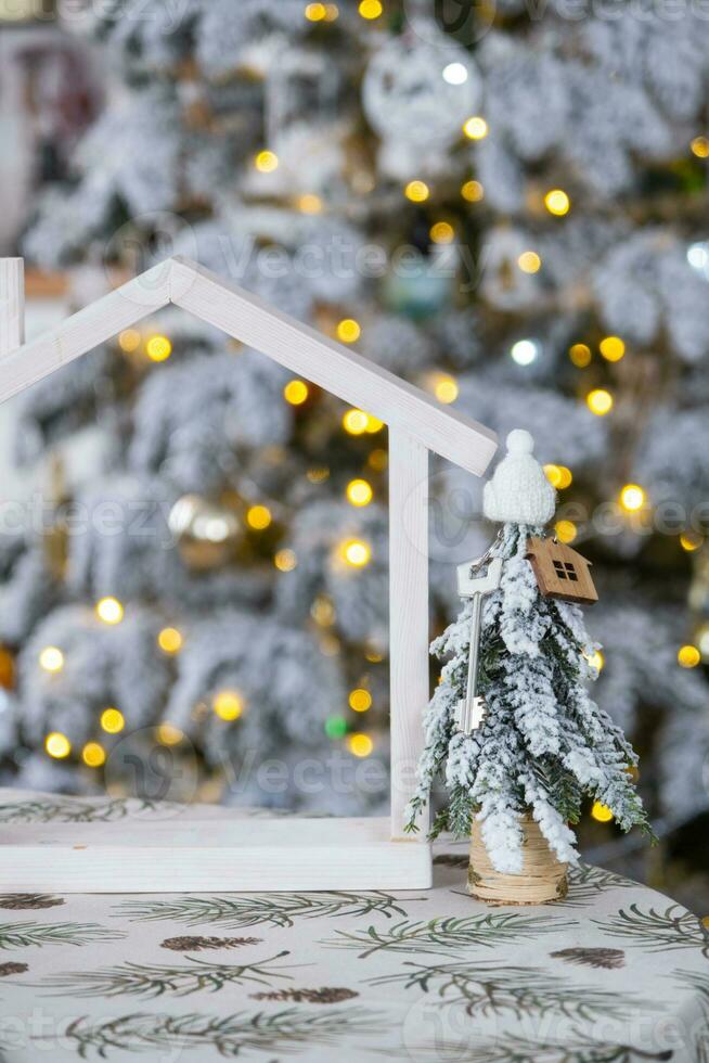 chiave su Natale albero e minuscolo Casa su accogliente casa con Natale arredamento su tavolo di festivo bianca cucina. regalo per nuovo anno. assicurazione, in movimento per nuovo Casa, mutuo, affitto e vero tenuta foto