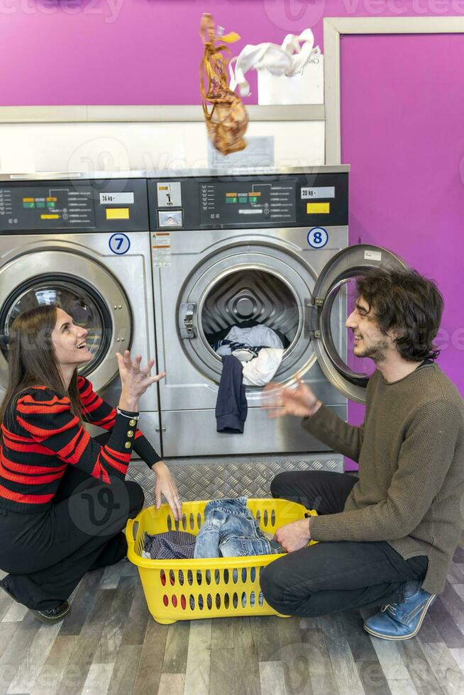 giovane coppia è mettendo Abiti nel il lavaggio macchina tamburo foto