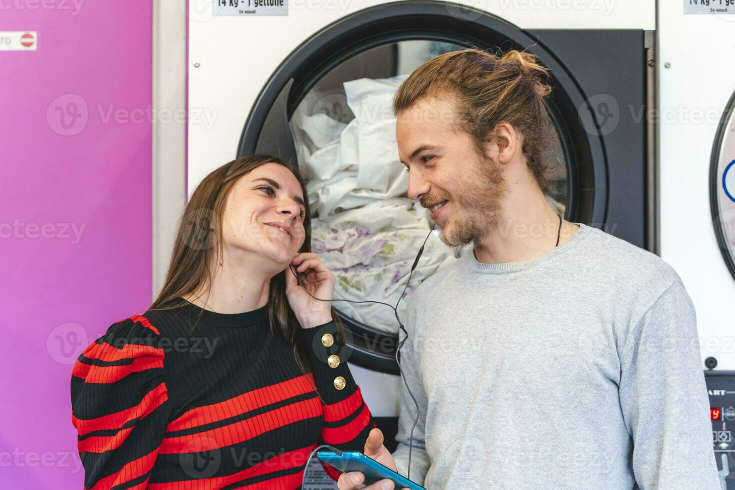 contento giovane coppia è ascoltando per musica a partire dal un' inteligente Telefono nel un' pubblico lavanderia foto