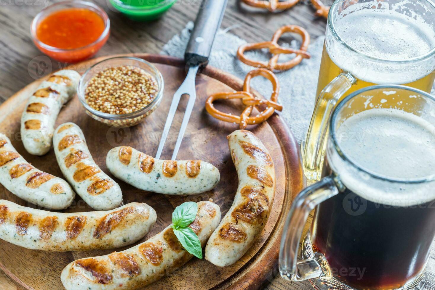 grigliato salsicce con salatini e tazze di birra foto