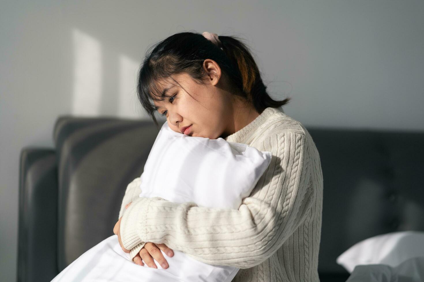 il triste e solitario donna è abbracciare un' cuscino su il letto nel il Camera da letto a casa. foto