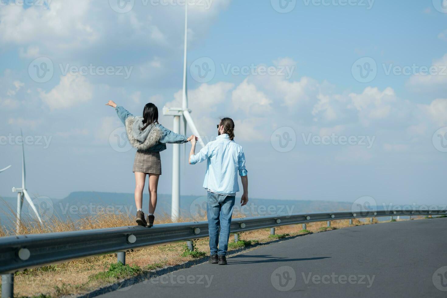 indietro Visualizza di giovane coppia a piedi su il strada con vento turbine nel sfondo foto