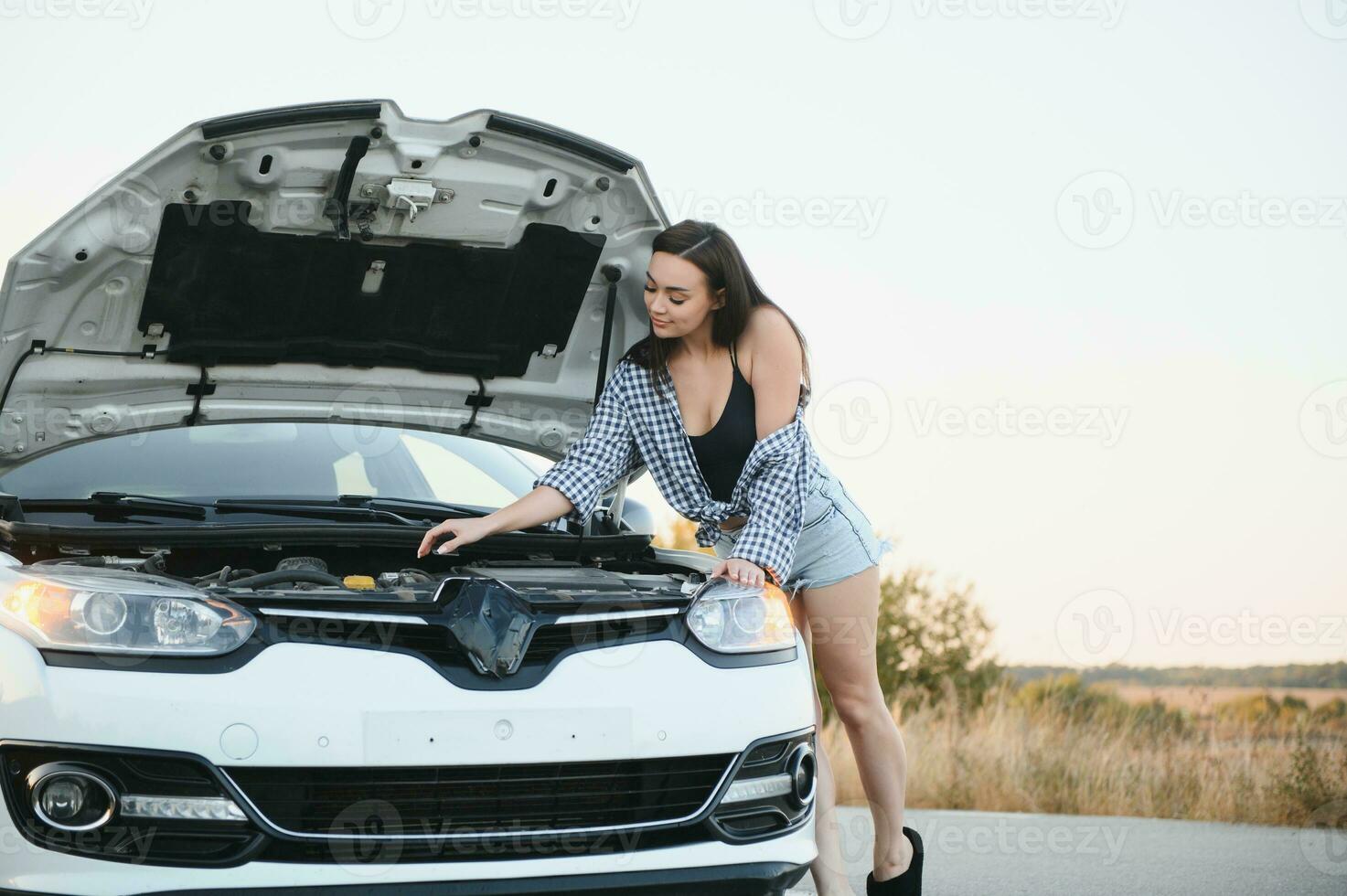 attraente sottile giovane ragazza nel estate pantaloncini e camicia riparazione un' rotto macchina. un' bellissimo donna sta vicino sollevato auto cappuccio. foto