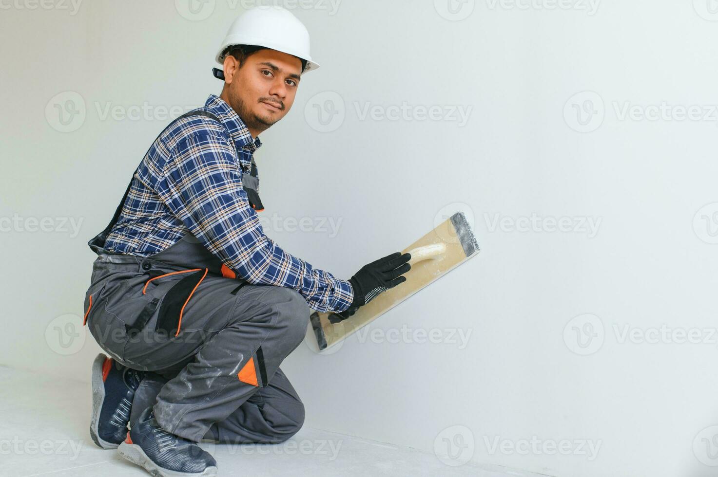 un indiano lavoratore lavori nel un vuoto appartamento. un' uomo nel un' uniforme fa riparazione dentro il edificio foto