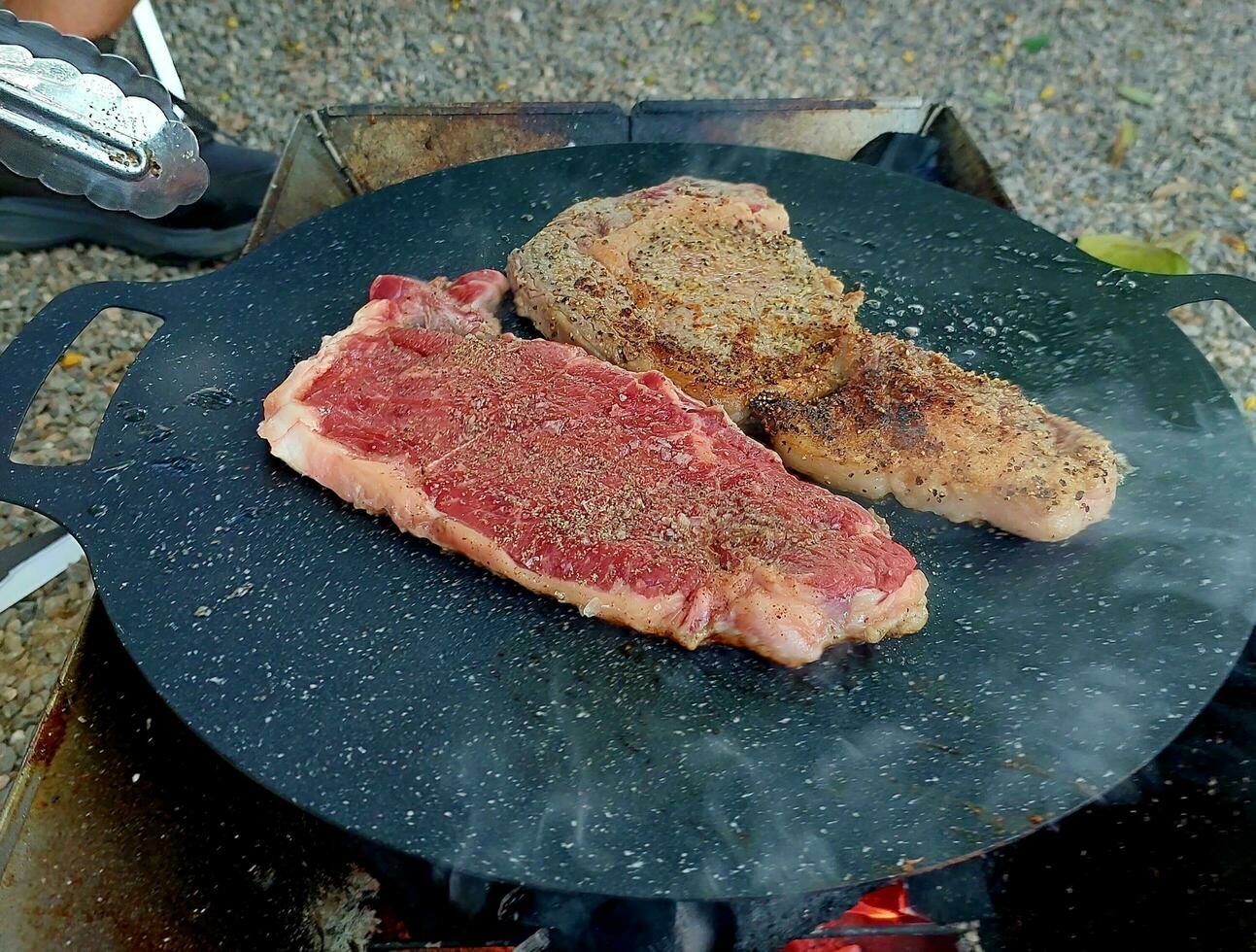 cucinando bistecche a campeggio. friggere bistecche nel un' frittura padella a campeggio. bistecche nel un' padella. Due Grasso succoso bistecca fritte nel il oliva olio nel un' frittura padella. foto