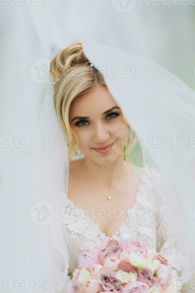 ritratto di il sposa. il sposa è in piedi con un' mazzo nel un' bianca vestito coperto con un' velo, nel un' verde campo. un' meraviglioso vestire. bella donna. nozze foto