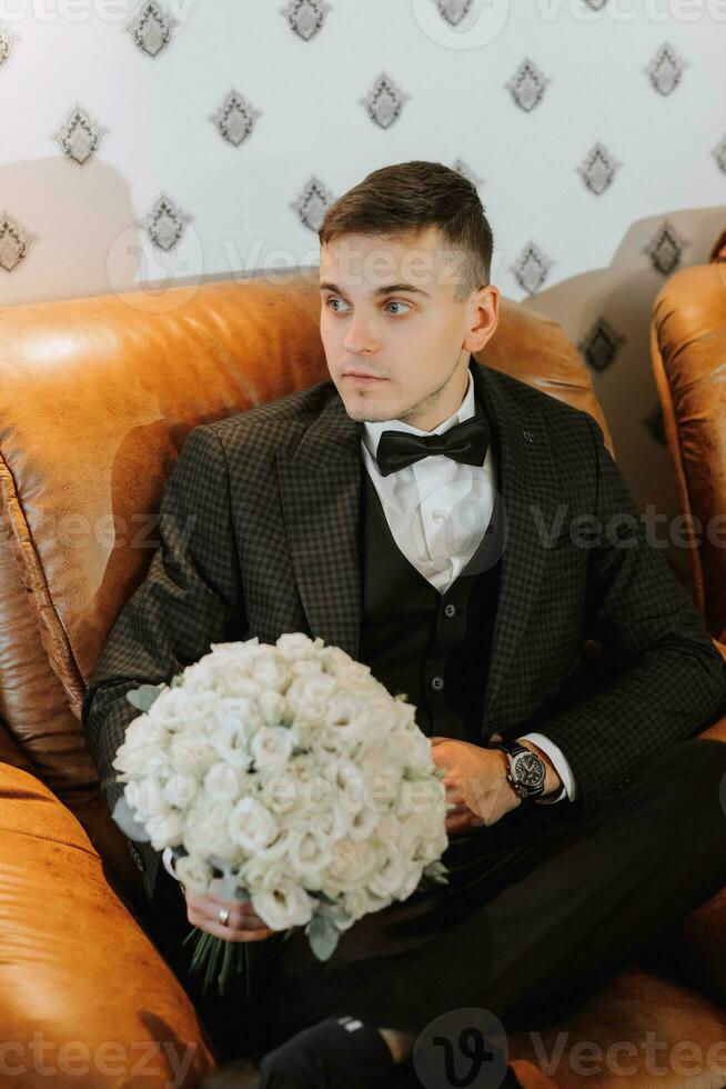 sposo con un' mazzo di fiori nel un' camera con un' meraviglioso interno. il sposo pose per il fotografo foto