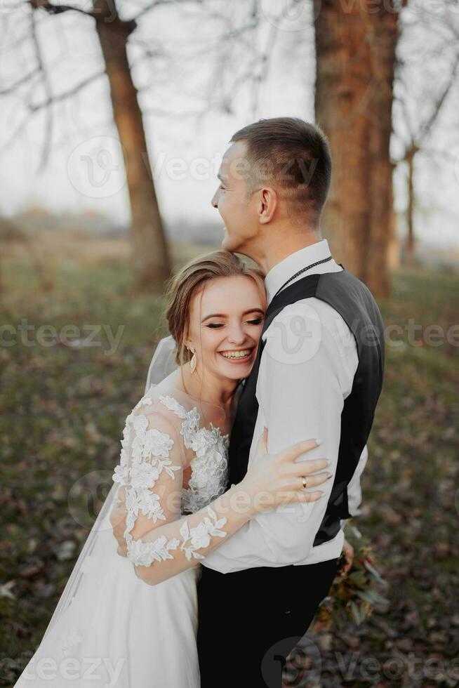 nozze foto. il sposa e sposo siamo a piedi nel il foresta. il sposo abbracci il le spalle di il suo Amati. lungo nozze vestire. un' coppia nel amore tra alto alberi. autunno luce del sole. foto