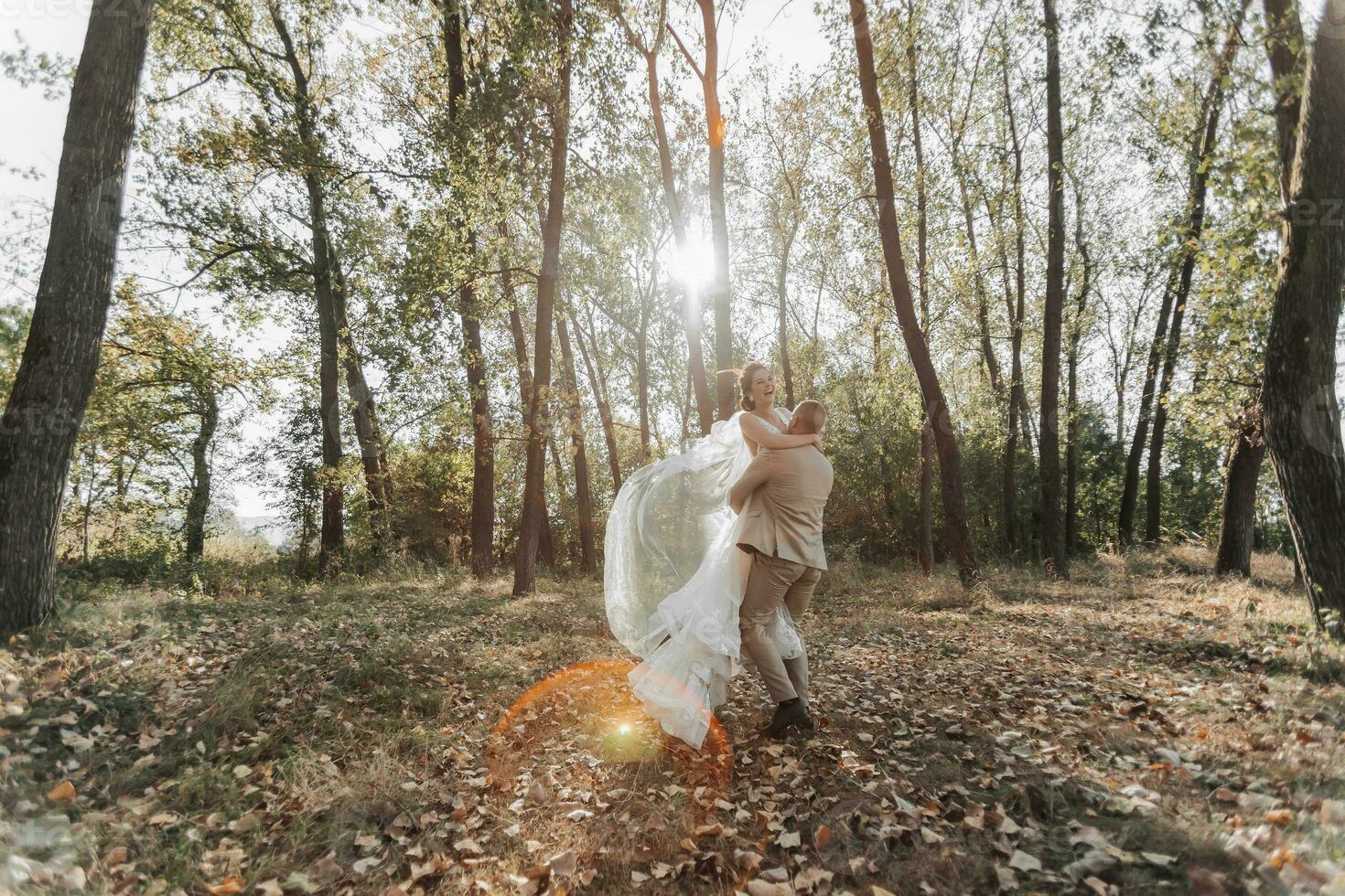 ritratto di contento sposa e sposo nel il foresta. il sposo detiene il sposa nel il suo braccia, danza con suo. un' lungo velo nel il aria. un' raggio di il sole nel il foto. largo angolo foto