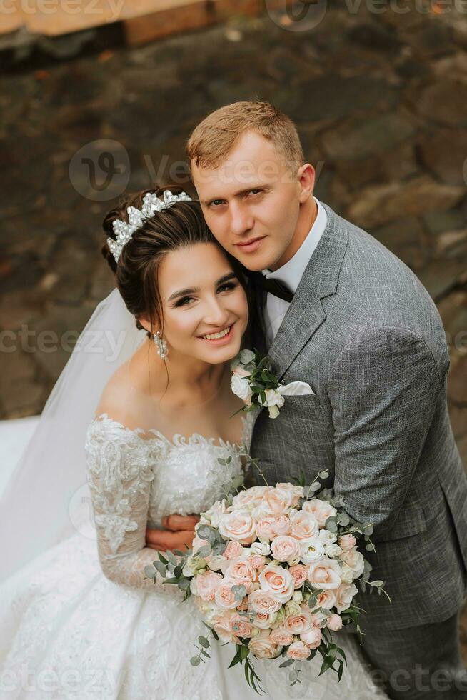 nozze foto. il sposa nel un' voluminoso bianca vestito e un' lungo velo sta con il sposo nel il parco su un' pietra sentiero. Visualizza a partire dal sopra. ritratto di il sposa. bellissimo riccioli. bellissimo trucco. foto