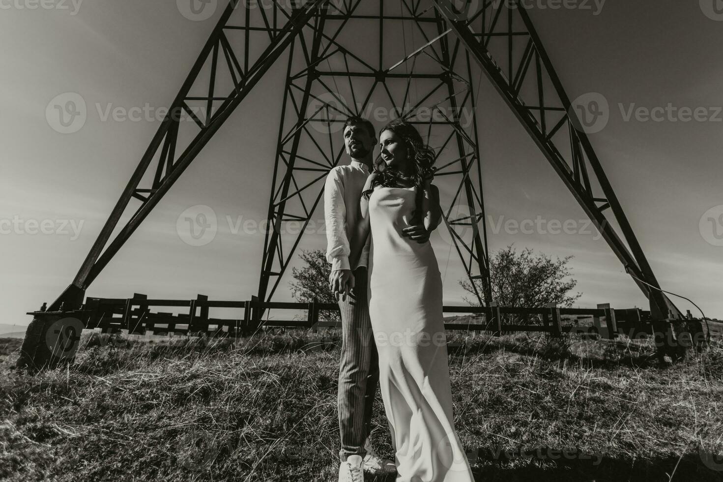 elegante modello coppia nel il montagne nel estate. un' giovane ragazzo e ragazza nel un' bianca seta vestito siamo in piedi vicino grande strutture di energia Linee. nero e bianca contrasto foto