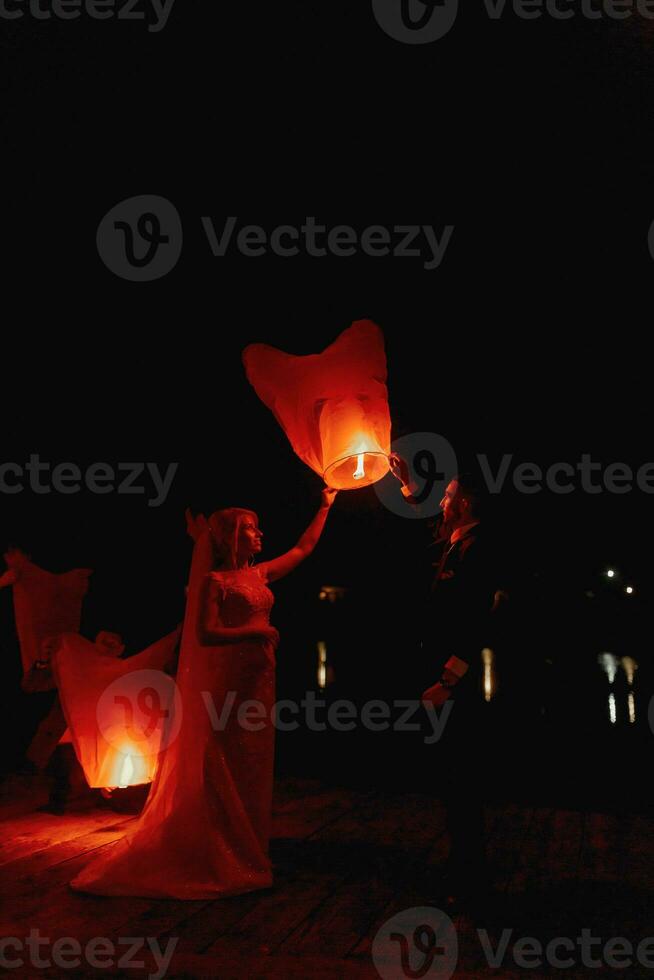 di recente sposato coppia Abbracciare una persona ogni altro con il rosso Cinese cielo lanterne nel il sfondo. foto