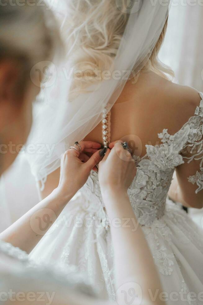 mattina sposa. damigella d'onore porzione il sposa allacciatura su sua vestire. amiche Aiuto il sposa per allacciare un' vestito foto