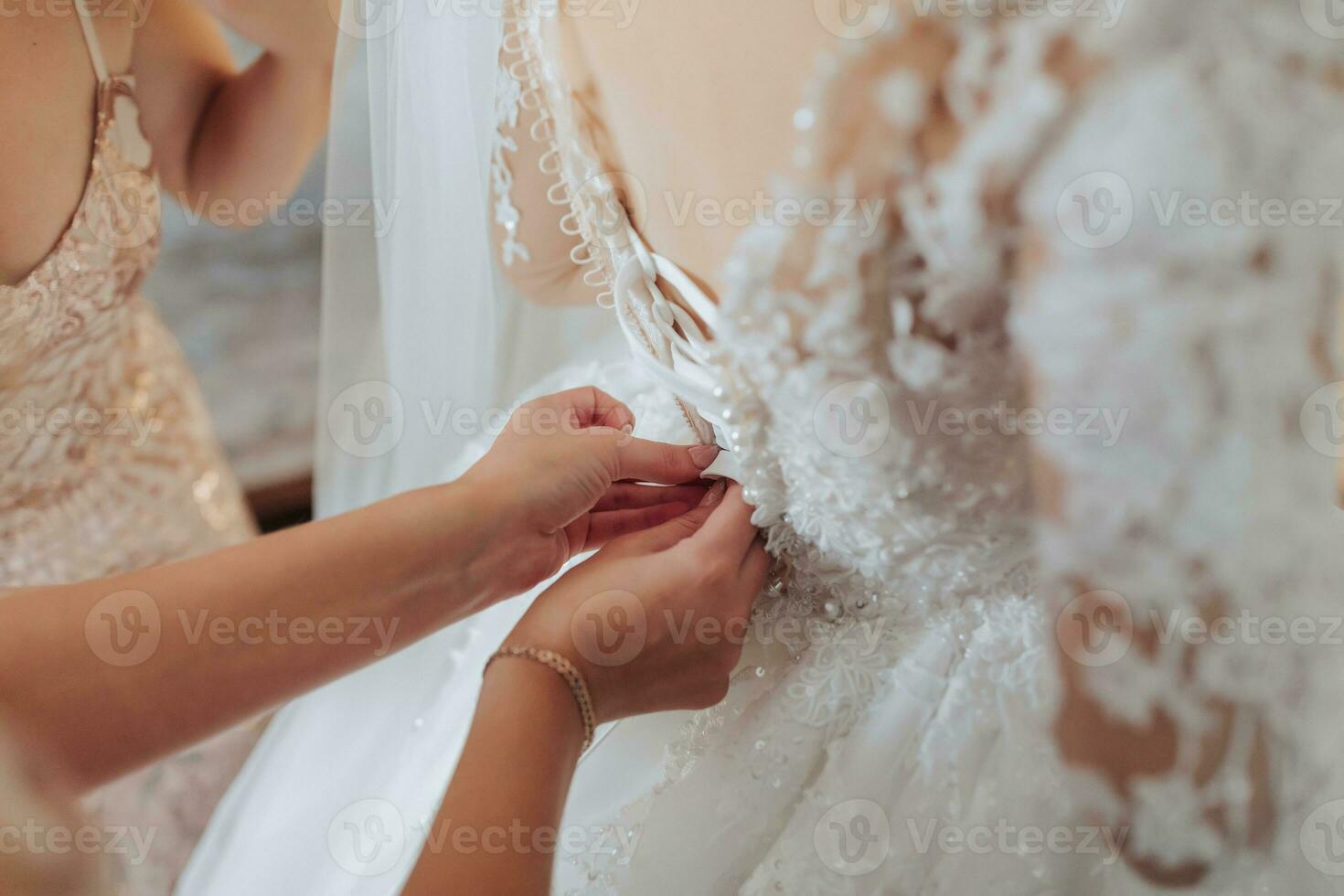 il della sposa amici allacciare il bianca voluminoso vestito di il sposa. posteriore Visualizza. Aperto le spalle. bellissimo mani. lungo velo. mattina di il sposa. foto