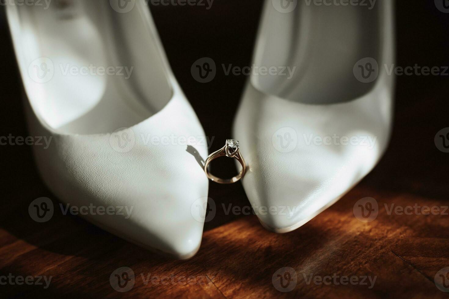foto di dettagli a il nozze. il nozze squillare di il sposa sta su bianca classico scarpe, quale siamo collocato su un' di legno sfondo. contorno linea. ombre e luce.