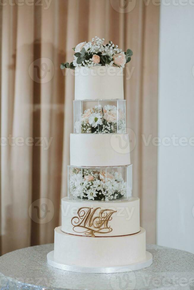 un' bianca nozze torta, decorato con rosa fiori, sta su un' bicchiere In piedi. fresco fiori per un' nozze. dolci foto