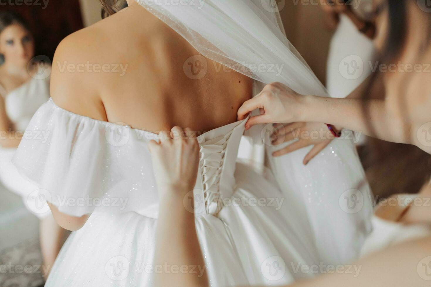 il della sposa amici allacciare il bianca voluminoso vestito di il sposa. posteriore Visualizza. Aperto le spalle. bellissimo mani. lungo velo. mattina di il sposa. foto