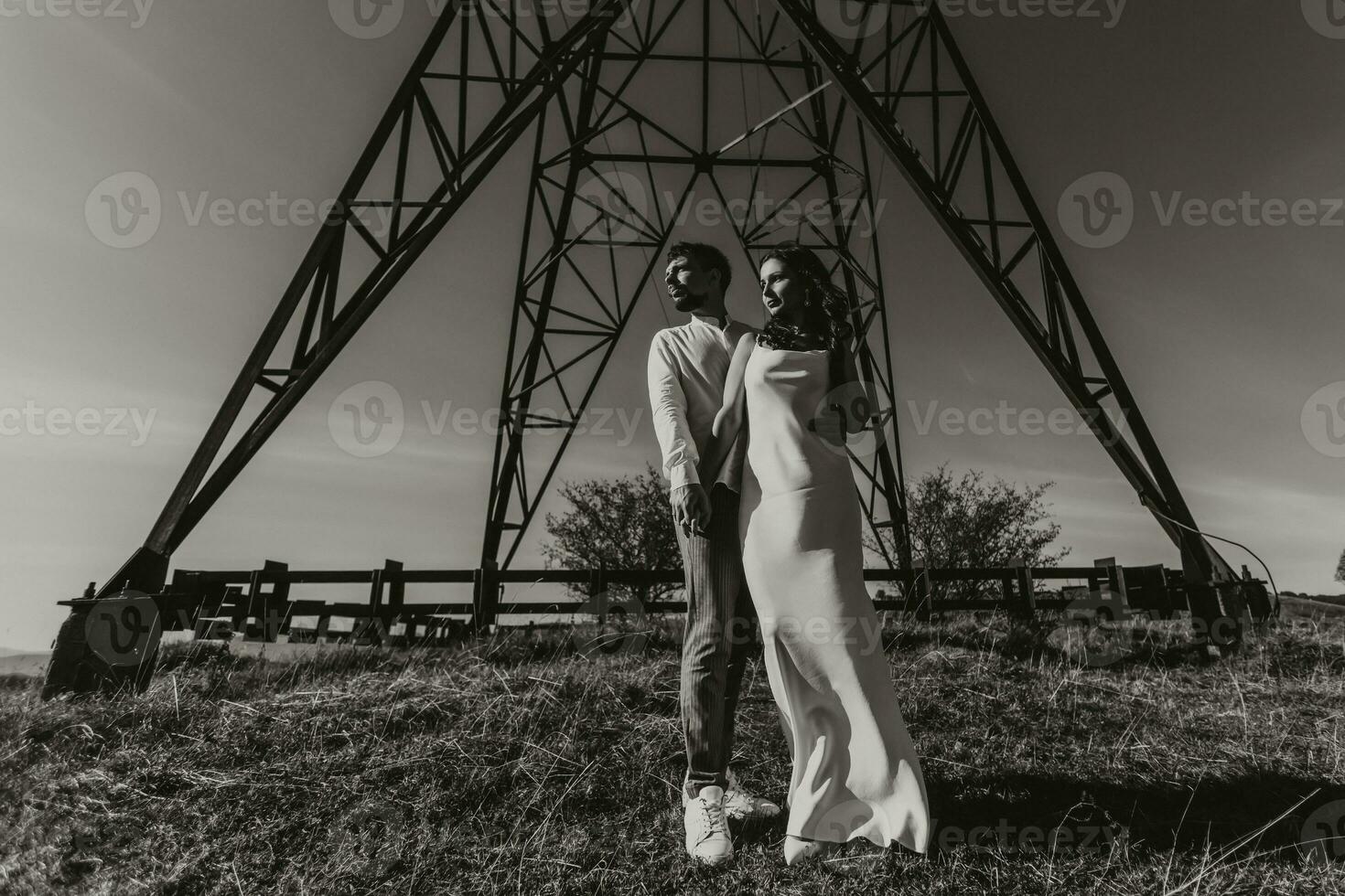 elegante modello coppia nel il montagne nel estate. un' giovane ragazzo e ragazza nel un' bianca seta vestito siamo in piedi vicino grande strutture di energia Linee. nero e bianca contrasto foto