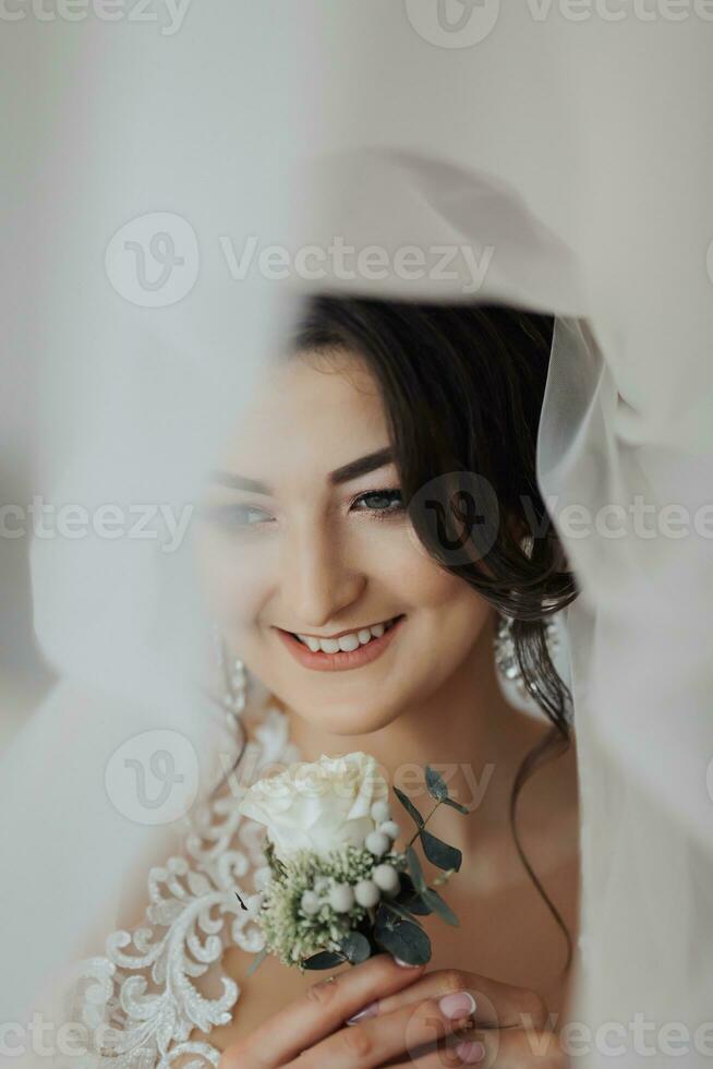 un' brunetta sposa nel un' bianca vestito detiene sua nozze mazzo, pose. francese manicure. Aperto le spalle. bellissimo mani. lungo velo. mattina di il sposa. dettagli foto