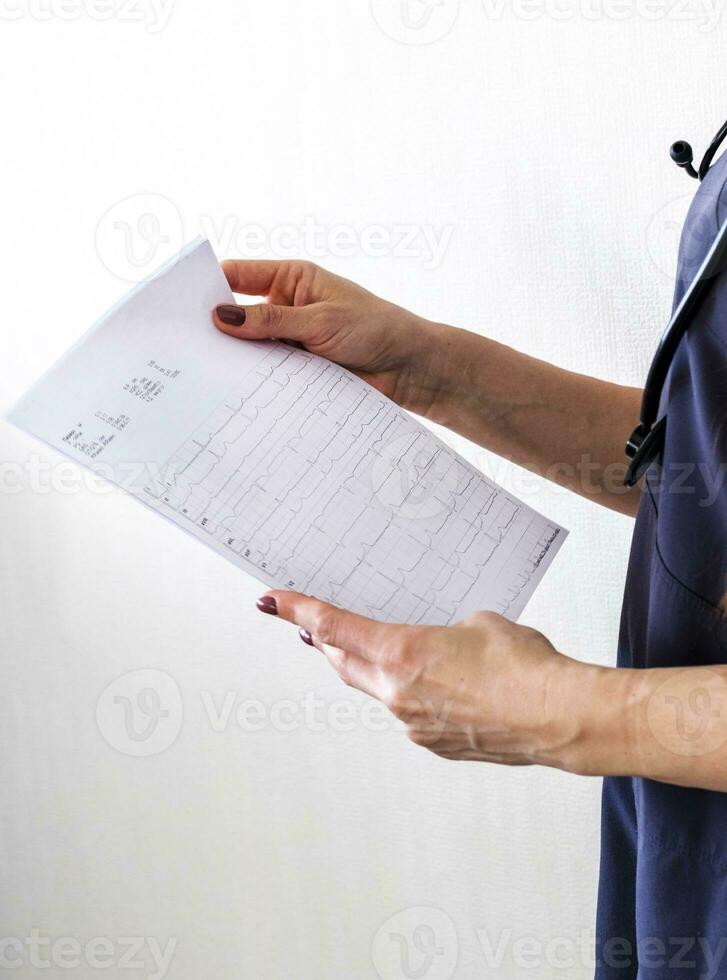 tiro di il femmina medico nel uniforme contro il bianca parete studiando cardiogramma. assistenza sanitaria foto