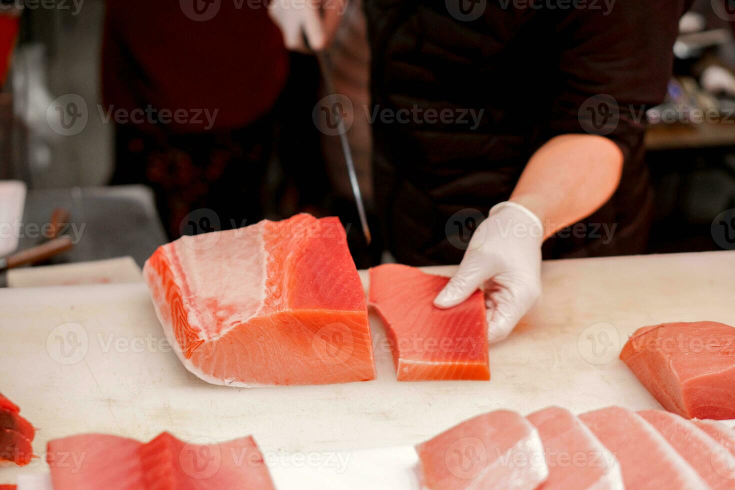 mani di giapponese capocuoco utilizzando capocuoco coltello affettato pezzo di fresco tonno pesce per vendere per cliente nel mattina pesce mercato, Giappone. foto