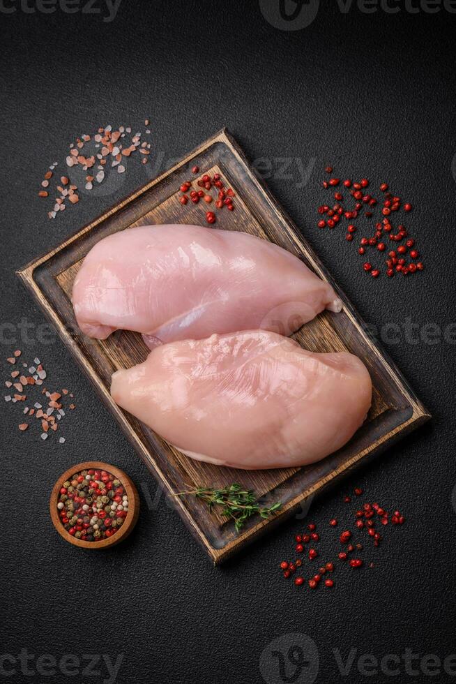 filetto di pollo fresco su un tavolo di cemento scuro con spezie ed erbe aromatiche foto