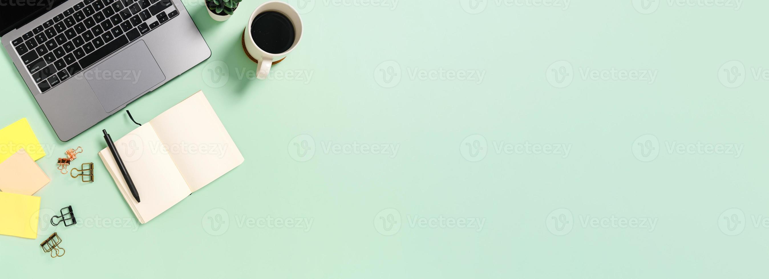 piatto creativo della scrivania dell'area di lavoro. scrivania da ufficio vista dall'alto con laptop, tazza di caffè e taccuino nero mockup aperto su sfondo verde. banner panoramico con copia spazio per testo e area pubblicitaria. foto