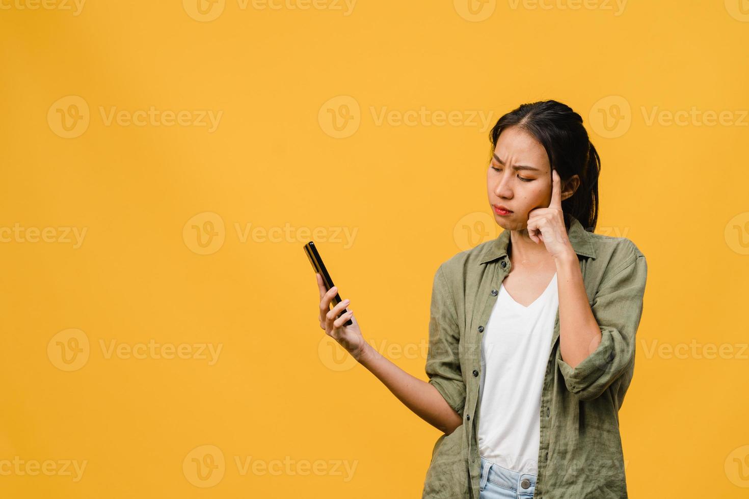 pensando di sognare la giovane donna asiatica che usa il telefono con espressione positiva, vestita con un panno casual sentendo felicità e stando isolata su sfondo giallo. felice adorabile donna felice esulta successo. foto