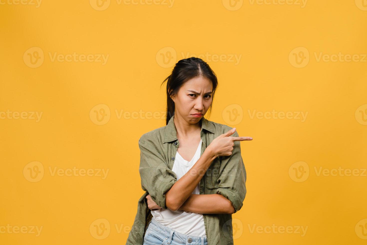 la giovane donna asiatica mostra qualcosa di straordinario nello spazio vuoto con espressione negativa, urla eccitate, pianto emotivo arrabbiato guardando la telecamera isolata su sfondo giallo. concetto di espressione facciale. foto