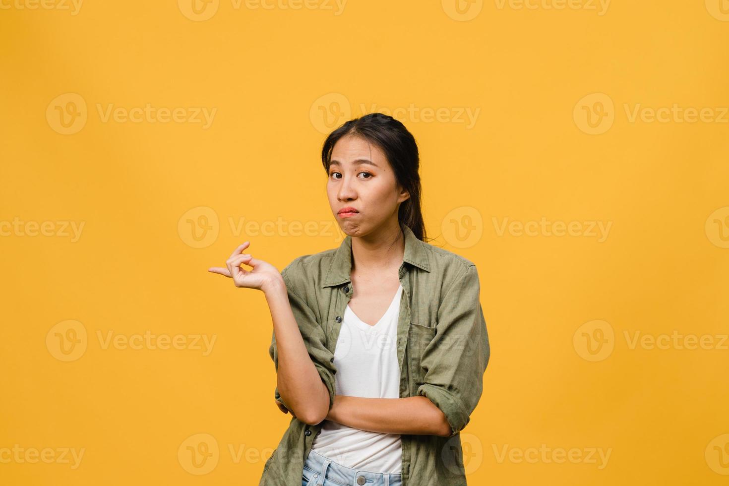 la giovane donna asiatica mostra qualcosa di straordinario nello spazio vuoto con espressione negativa, urla eccitate, pianto emotivo arrabbiato guardando la telecamera isolata su sfondo giallo. concetto di espressione facciale. foto