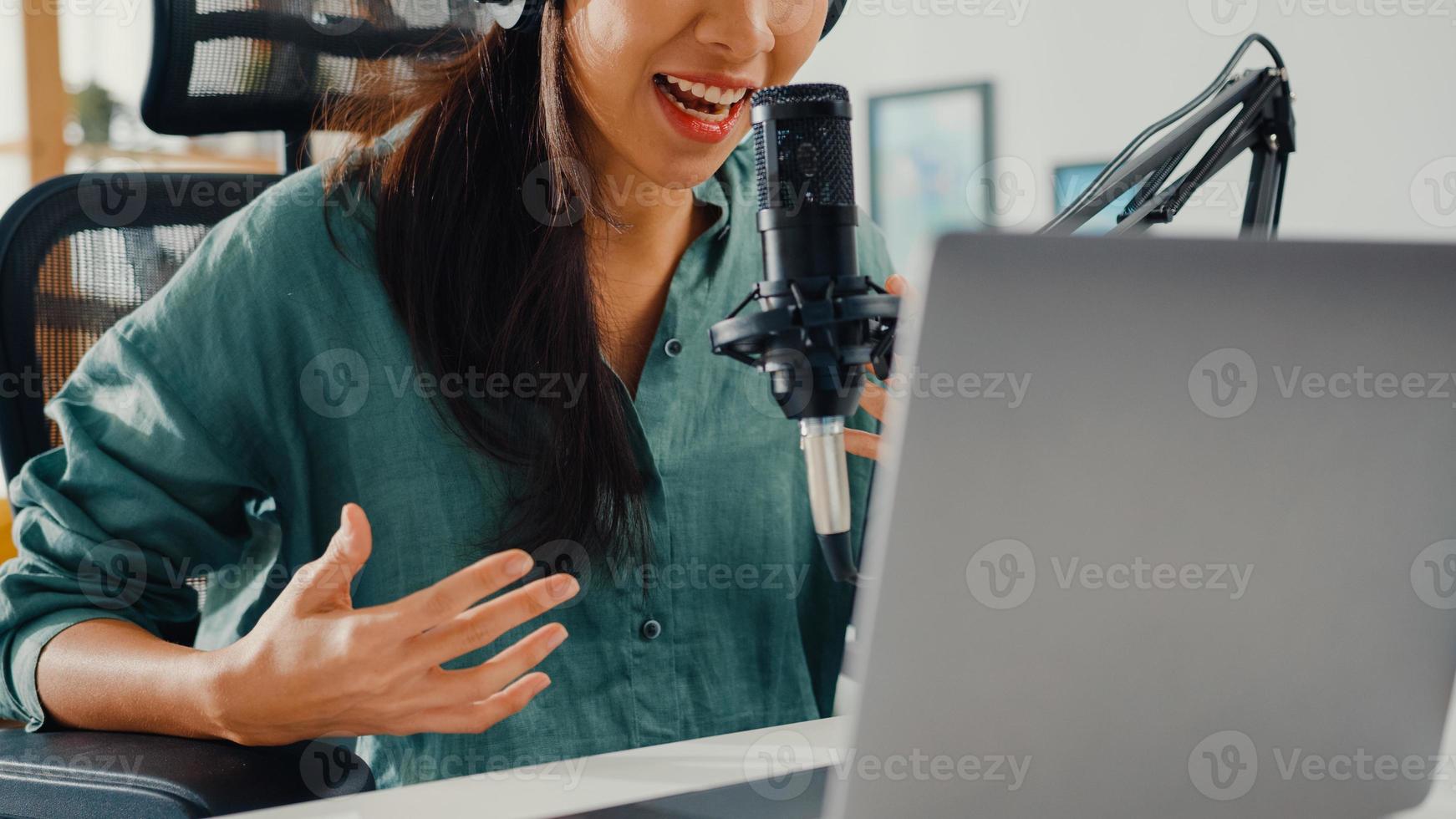 felice ragazza asiatica registra un podcast sul suo computer portatile con cuffie e microfono parla con il pubblico nella sua stanza. il podcaster femminile crea podcast audio dal suo studio di casa, resta al concetto di casa. foto