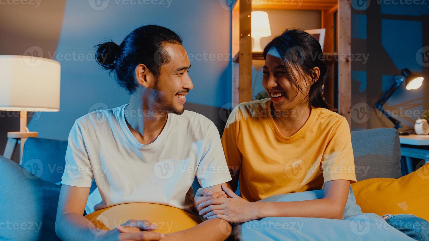 felice giovane coppia asiatica uomo e donna che guarda la macchina fotografica sorridere e allegro durante la videochiamata online di notte nel soggiorno di casa, stare a casa in quarantena, vita coniugale, concetto di distanza sociale. foto