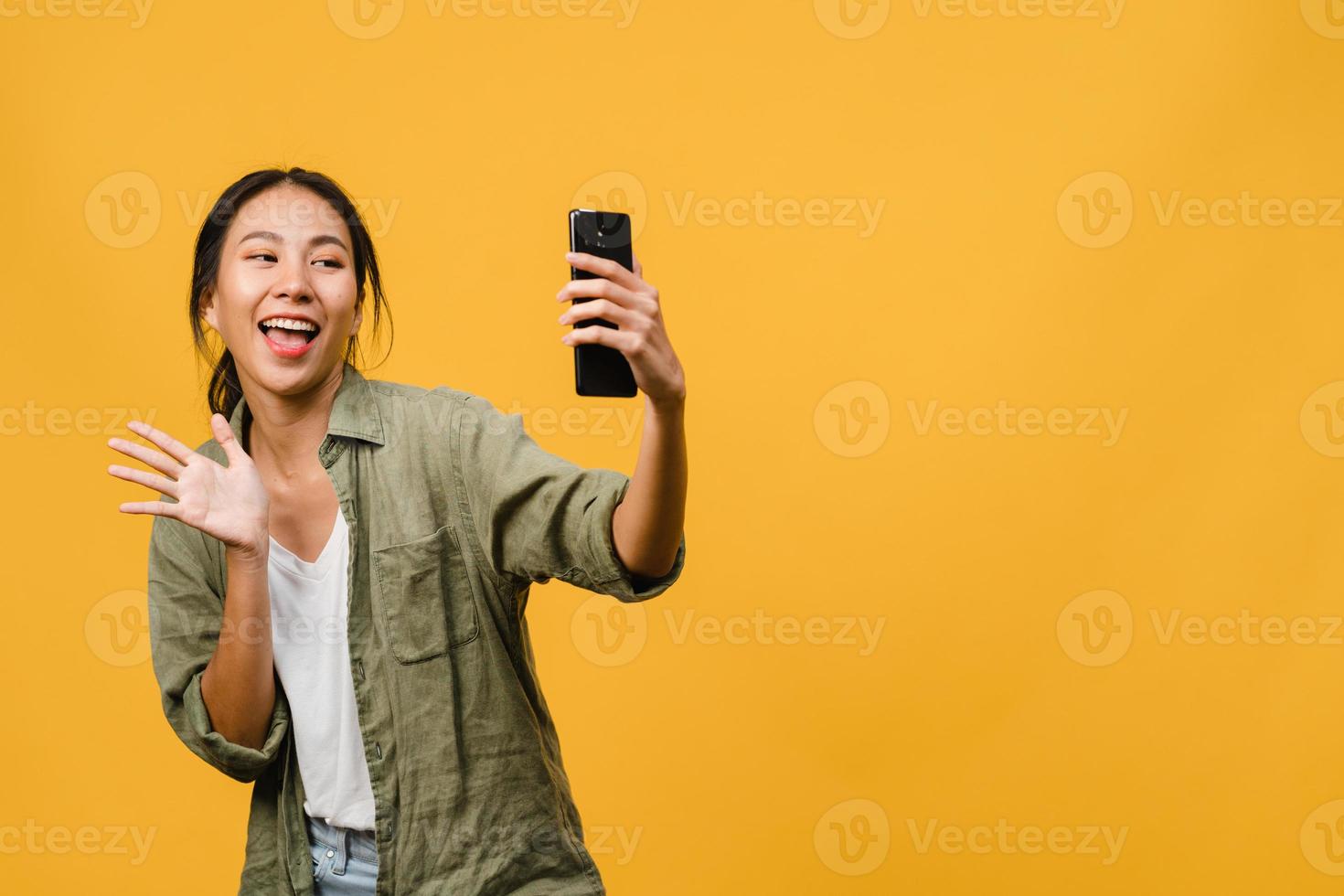 sorridente adorabile femmina asiatica che fa selfie foto su smart phone con espressione positiva in abbigliamento casual e stand isolato su sfondo giallo. felice adorabile donna felice esulta successo.