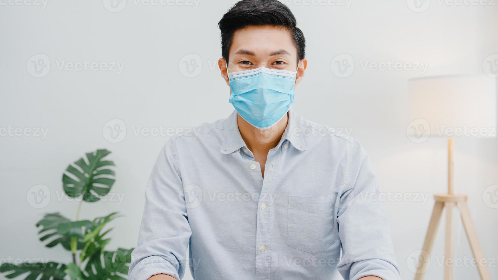 uomo d'affari asiatico indossare maschera facciale distanza sociale in situazione per la prevenzione dei virus guardando la telecamera sorridente sotto maschera chirurgica torna al lavoro nell'area di lavoro dell'ufficio. stile di vita dopo il virus corona. foto