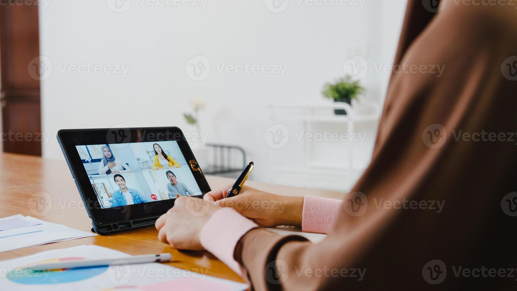 asia signora musulmana che utilizza tablet digitale parla con un collega del piano tramite videochiamata brainstorming riunione online mentre lavora in remoto da casa in soggiorno. distanziamento sociale, quarantena per il virus corona. foto