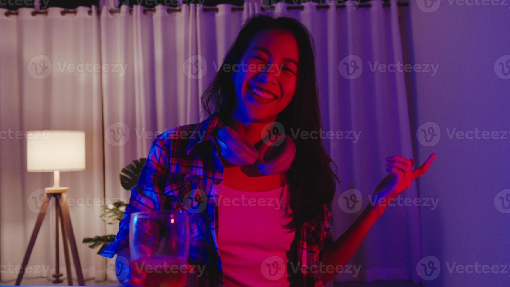 giovane signora asiatica che beve birra divertendosi momento felice discoteca neon night party evento celebrazione online tramite videochiamata nel soggiorno di casa. distanziamento sociale, quarantena per la prevenzione del coronavirus. foto