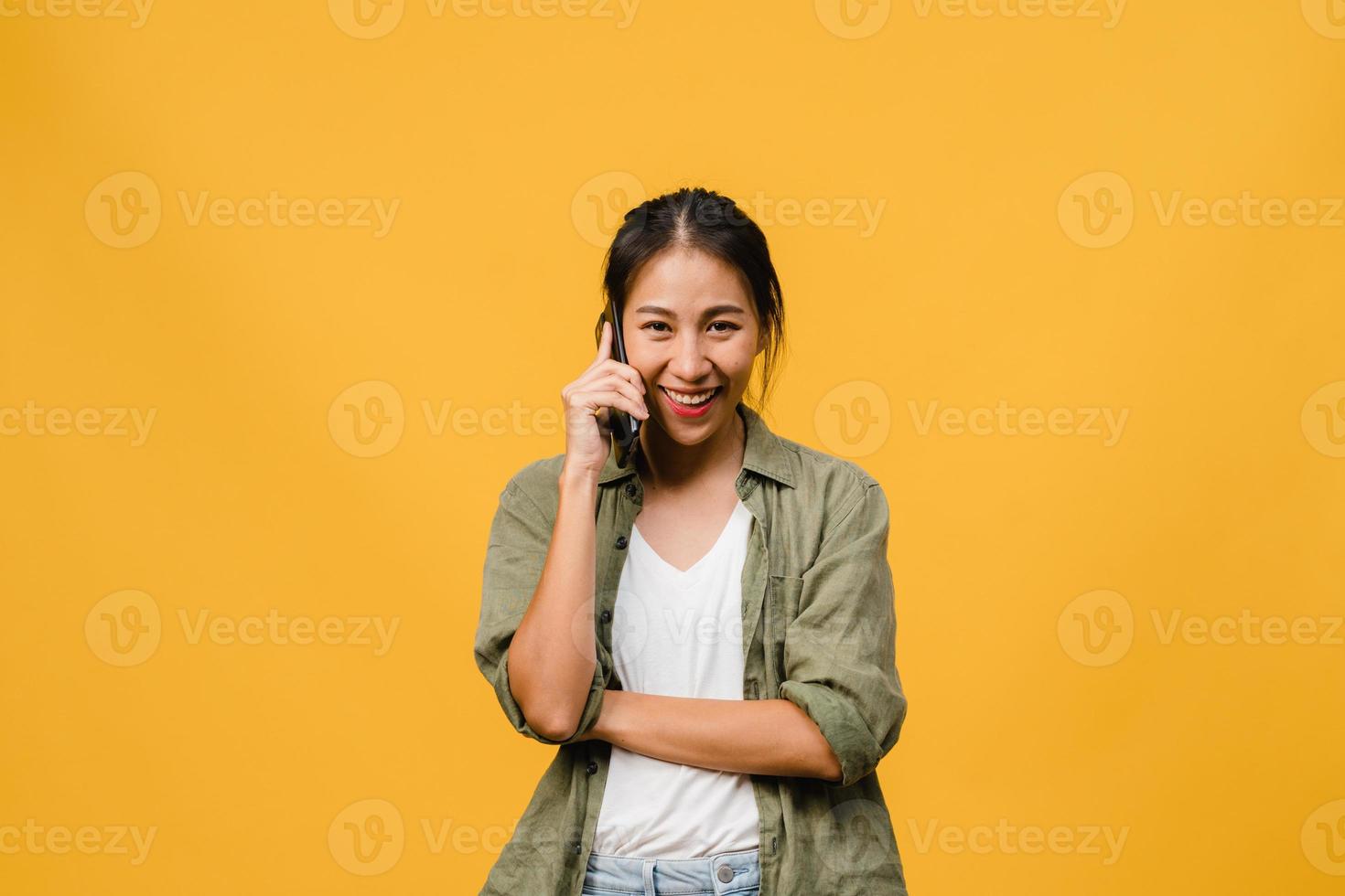 la giovane signora asiatica parla al telefono con un'espressione positiva, sorride ampiamente, vestita con abiti casual sentendo felicità e stando isolata su sfondo giallo. felice adorabile donna felice esulta successo. foto