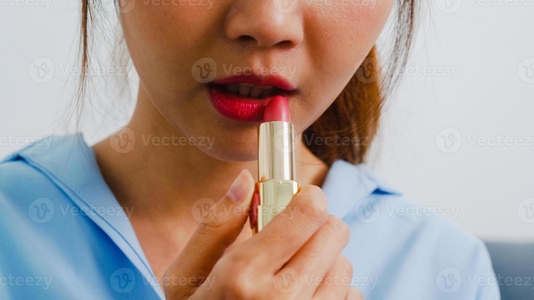 giovane donna asiatica che usa il rossetto si trucca davanti allo specchio, donna felice che usa cosmetici di bellezza per migliorarsi pronta a lavorare in camera da letto a casa. donne di stile di vita a casa concetto. foto