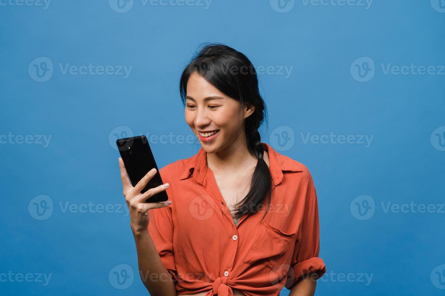 giovane donna asiatica che usa il telefono con un'espressione positiva, sorride ampiamente, vestita con abiti casual sentendosi felici e in piedi isolato su sfondo blu. felice adorabile donna felice esulta successo. foto