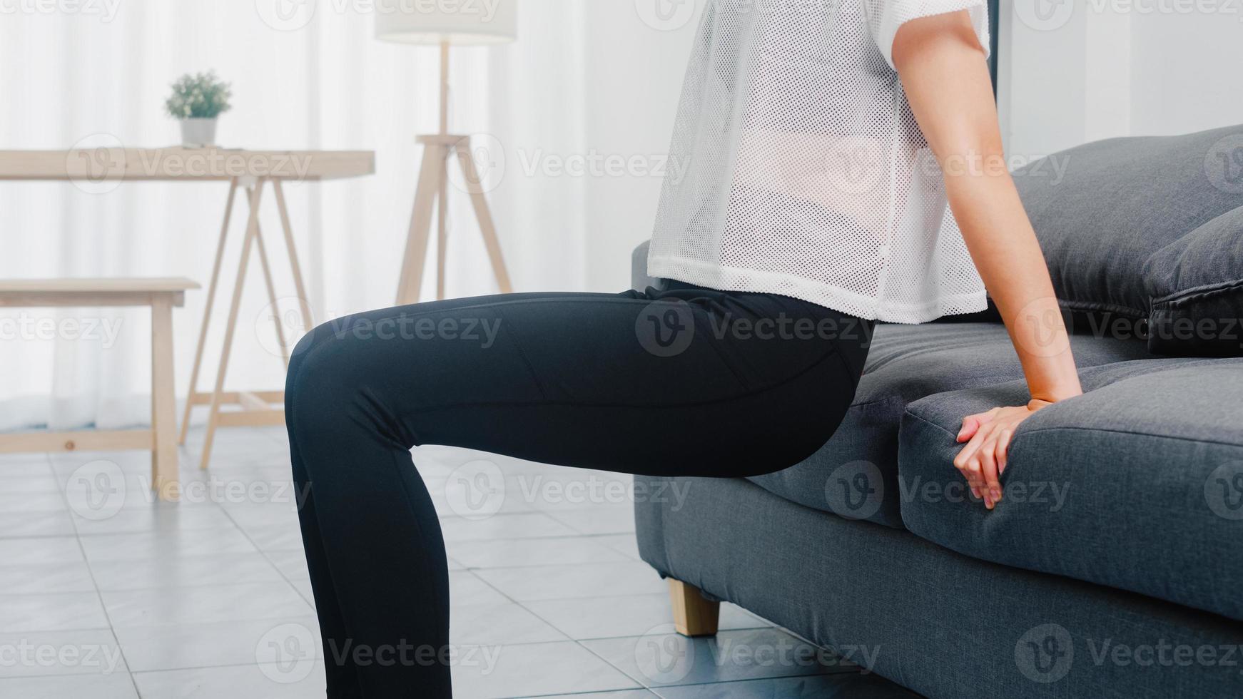 giovane donna coreana in esercizi di abbigliamento sportivo facendo allenamento facendo tuffi tricipiti appoggiata sul divano nel soggiorno di casa. distanza sociale, isolamento durante il virus. esercizi per la parte inferiore del corpo. foto