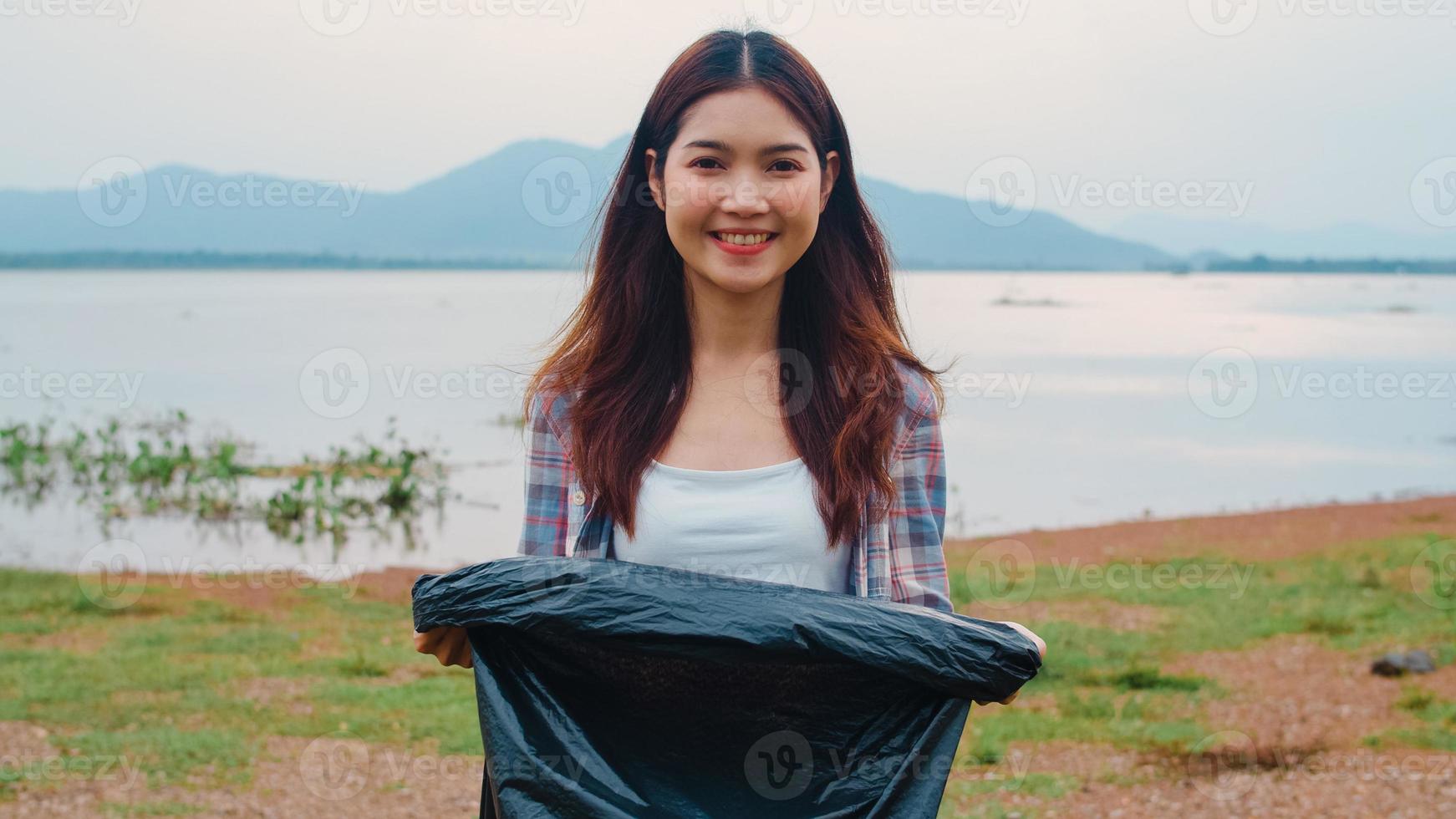 il ritratto di una giovane donna asiatica volontaria aiuta a mantenere la natura pulita guardando la macchina fotografica e sorride con i sacchetti della spazzatura neri sulla spiaggia. concetto sui problemi di inquinamento di conservazione ambientale. foto
