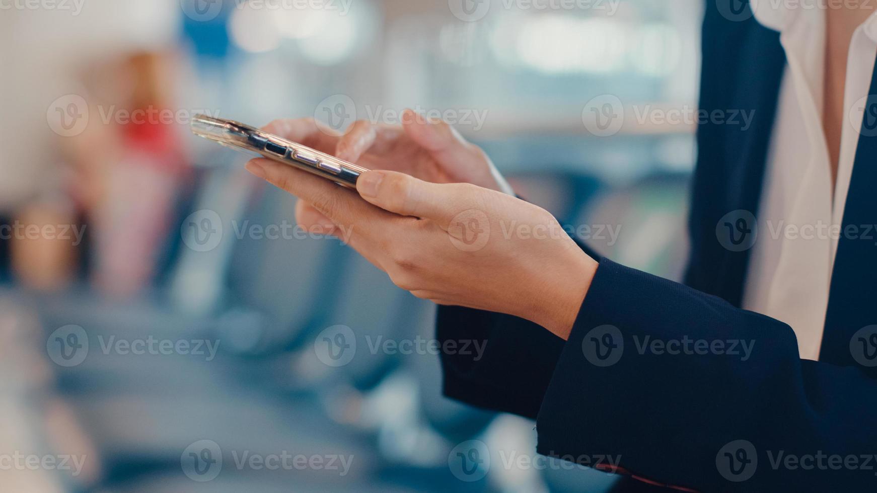 primo piano asiatico donna d'affari viaggiatore indossare abito seduto in panchina utilizzare smart phone prenotazione biglietto attendere il volo in aeroporto. pendolare di viaggio d'affari nella pandemia di covid, concetto di viaggio d'affari. foto