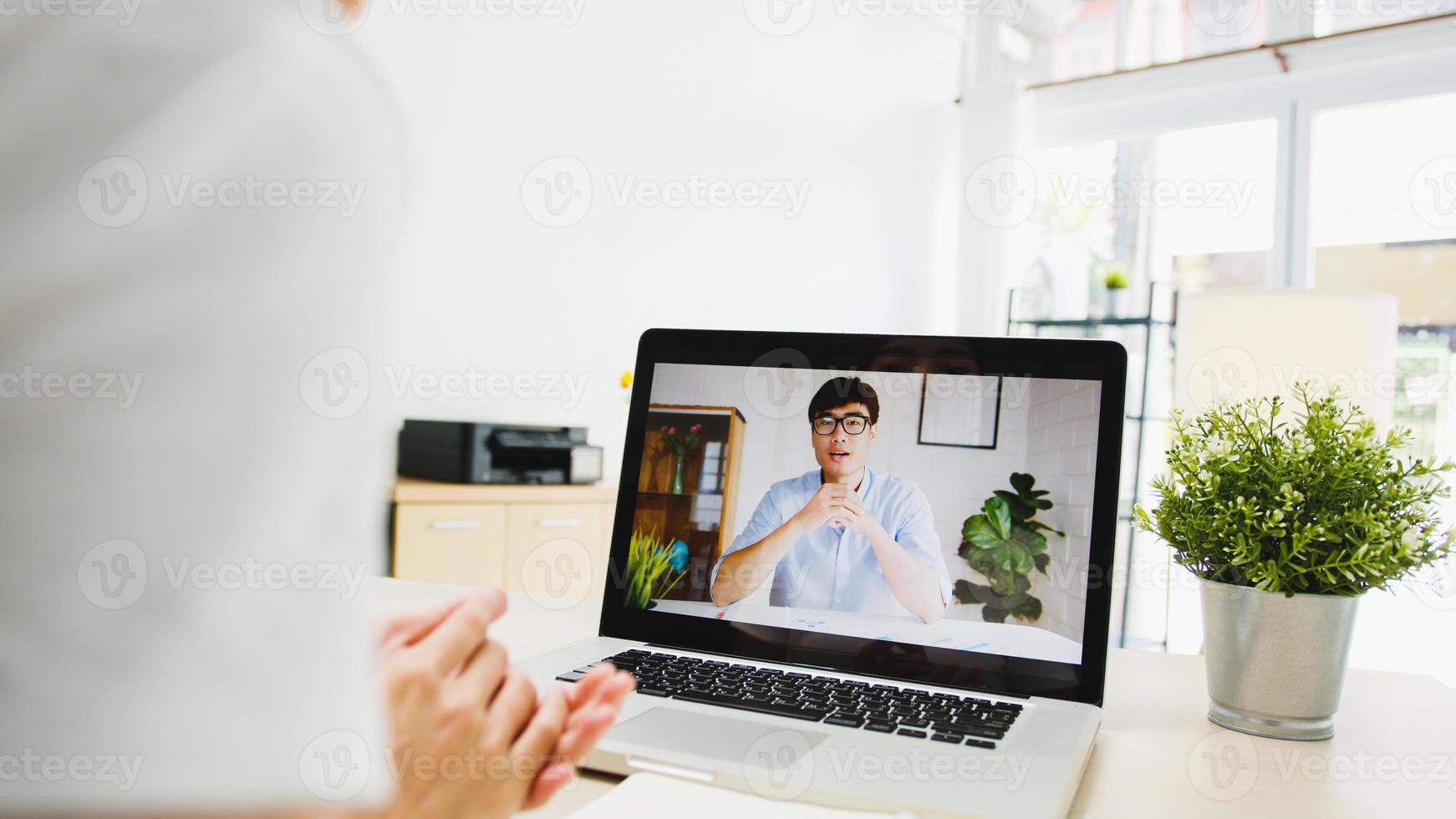 asia imprenditrice utilizzando laptop parlare con i colleghi del piano in videochiamata riunione mentre si lavora da casa in soggiorno. autoisolamento, distanziamento sociale, quarantena per la prevenzione del virus corona. foto