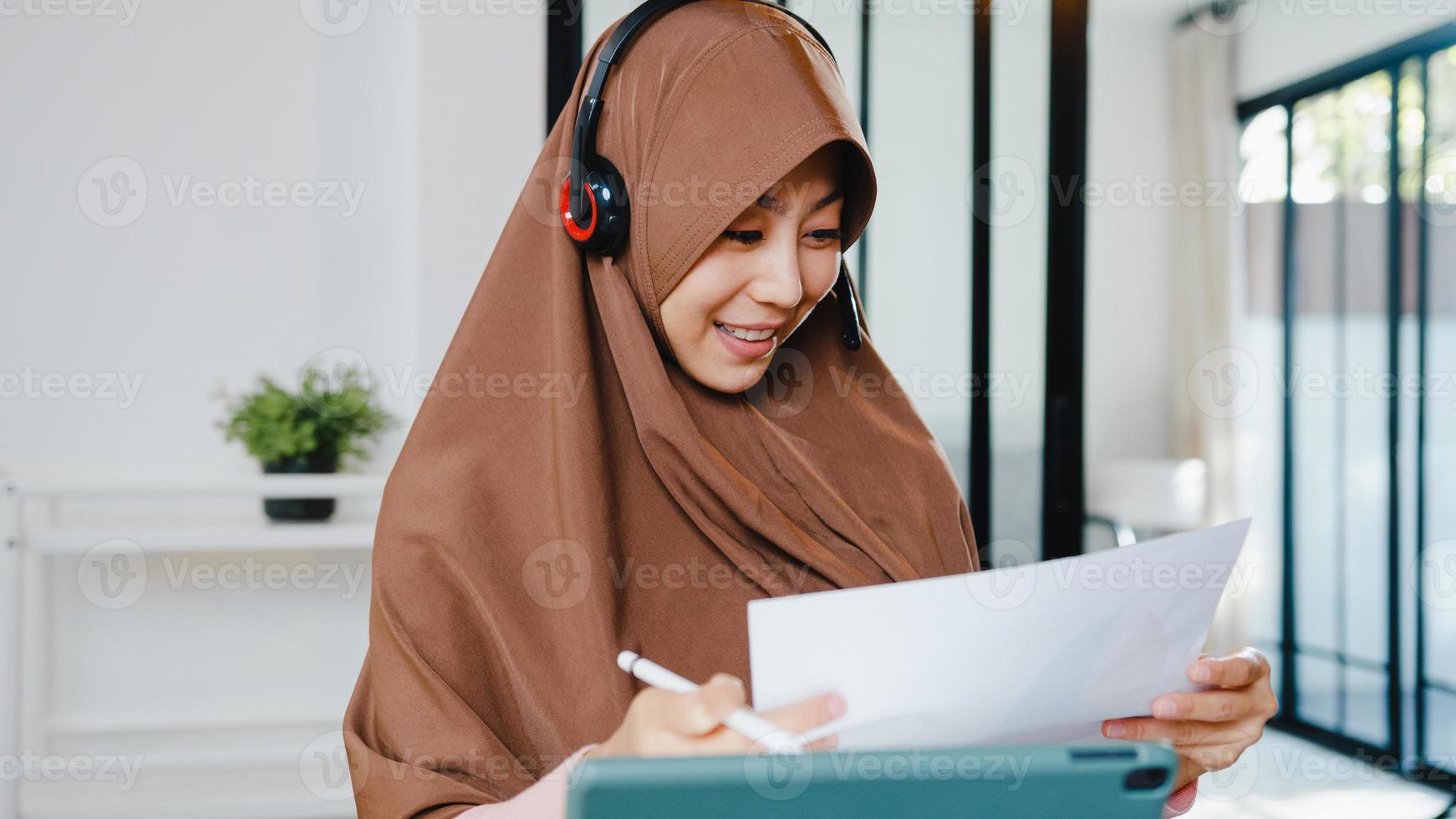 la signora musulmana asiatica indossa le cuffie utilizzando il tablet digitale parla con i colleghi del rapporto di vendita nella videochiamata in conferenza mentre si lavora da casa in cucina. distanziamento sociale, quarantena per il virus corona. foto