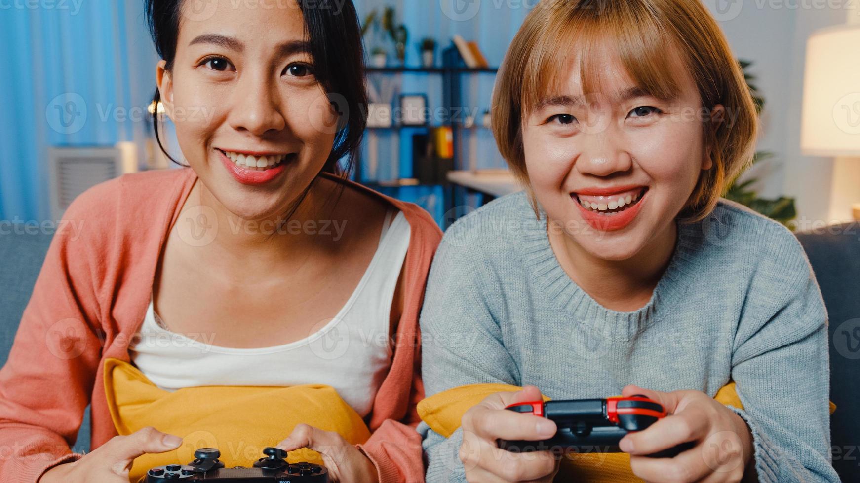 coppia di donne lesbiche lgbtq gioca a un videogioco a casa. giovane donna asiatica che utilizza un controller wireless che ha un momento felice e divertente sul divano nel soggiorno di notte. si divertono molto e festeggiano le vacanze. foto