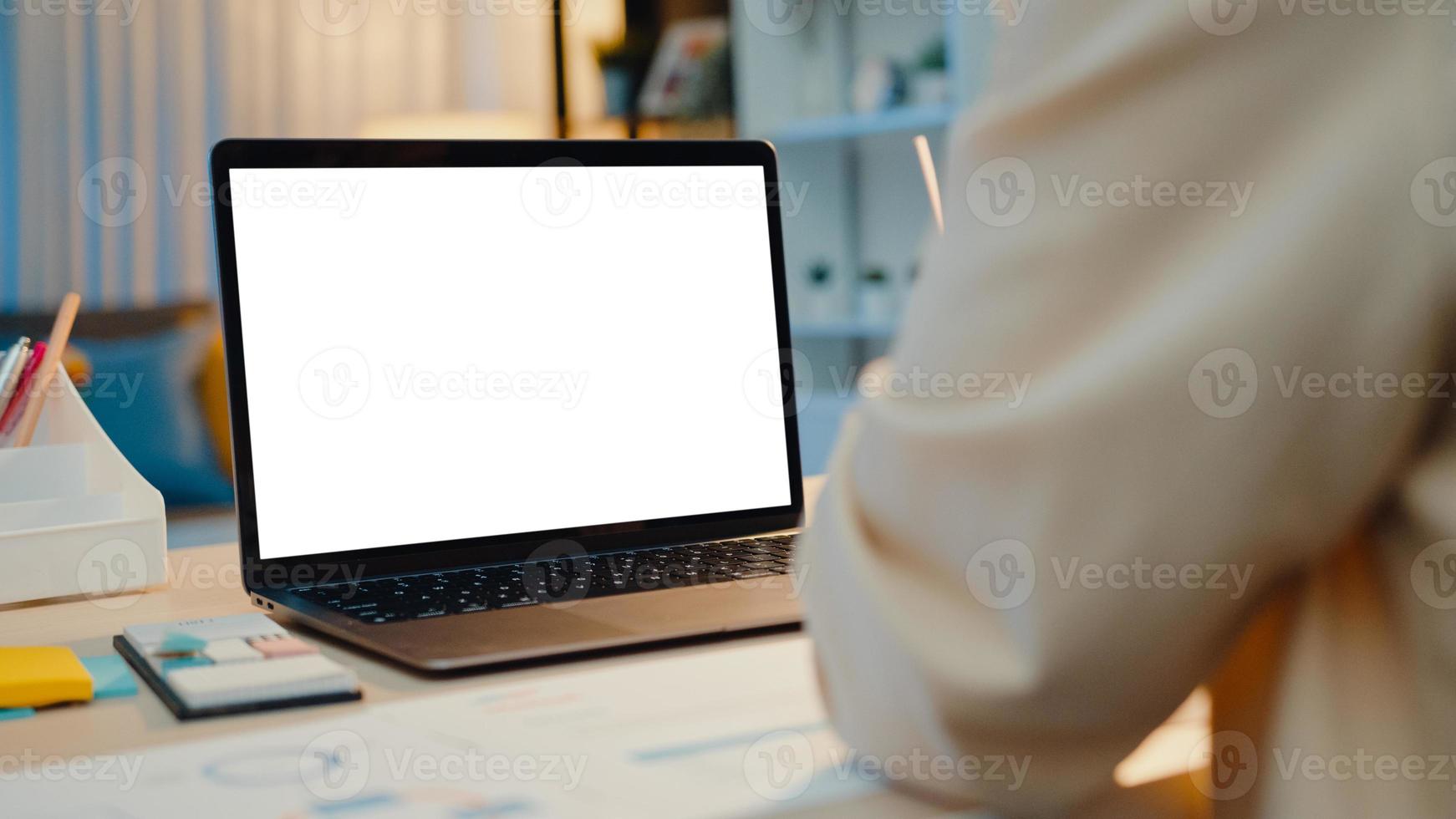 donna d'affari asiatica che utilizza laptop con schermo bianco vuoto mock up display per testo pubblicitario parla con i colleghi del piano in videochiamata riunione nel soggiorno di casa. sovraccarico di lavoro notturno. foto