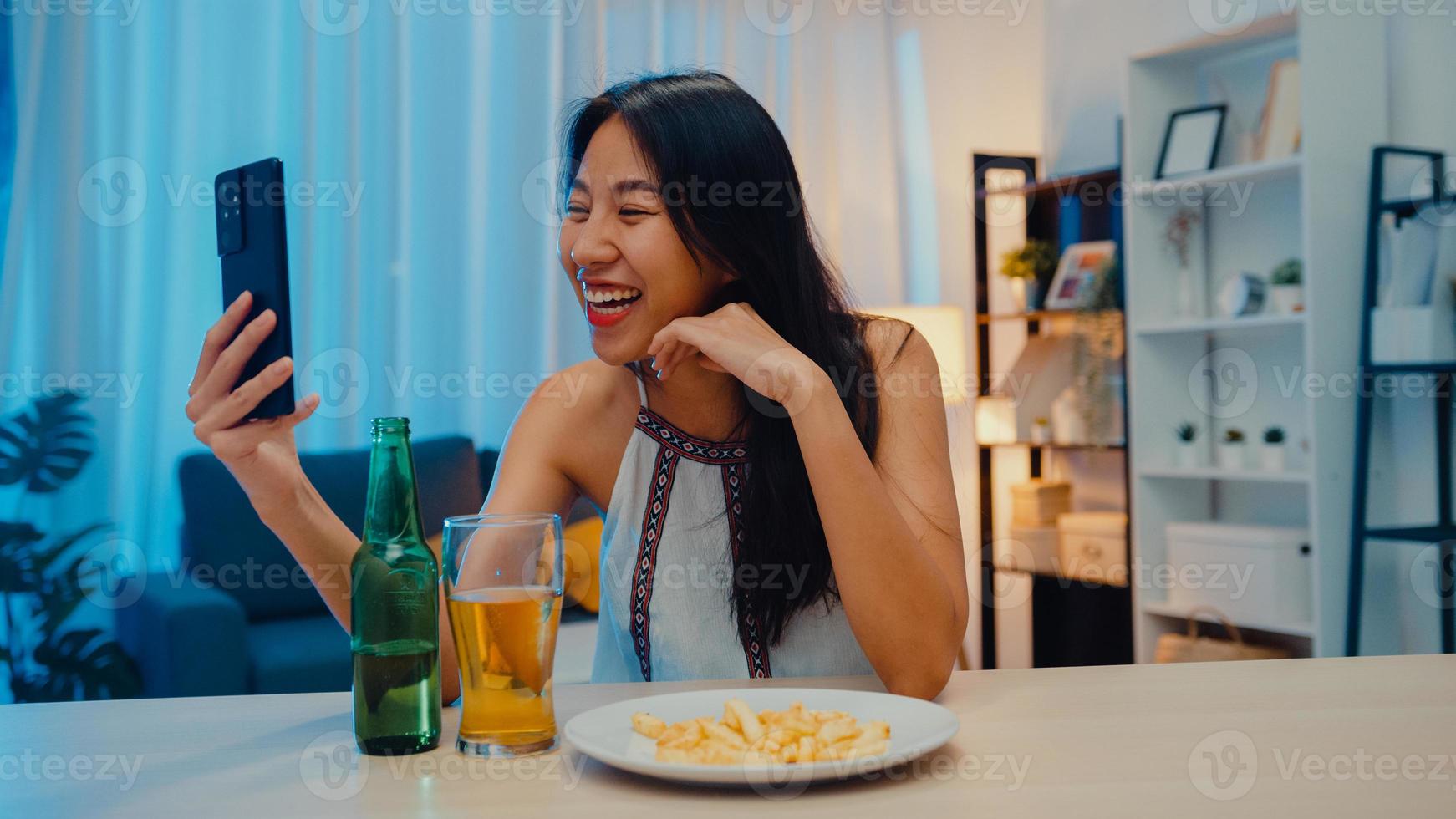 giovane signora asiatica che beve birra divertendosi momento felice festa notturna evento di capodanno celebrazione online tramite videochiamata per telefono a casa di notte. distanziamento sociale, quarantena per la prevenzione del coronavirus. foto