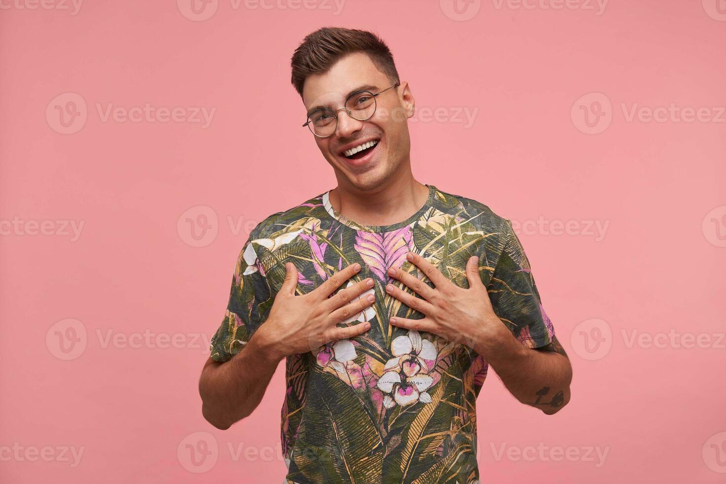 interno tiro di bello contento tipo, guardare a telecamera, guardare gioioso e felice, toccante se stesso con palme, isolato al di sopra di rosa sfondo foto